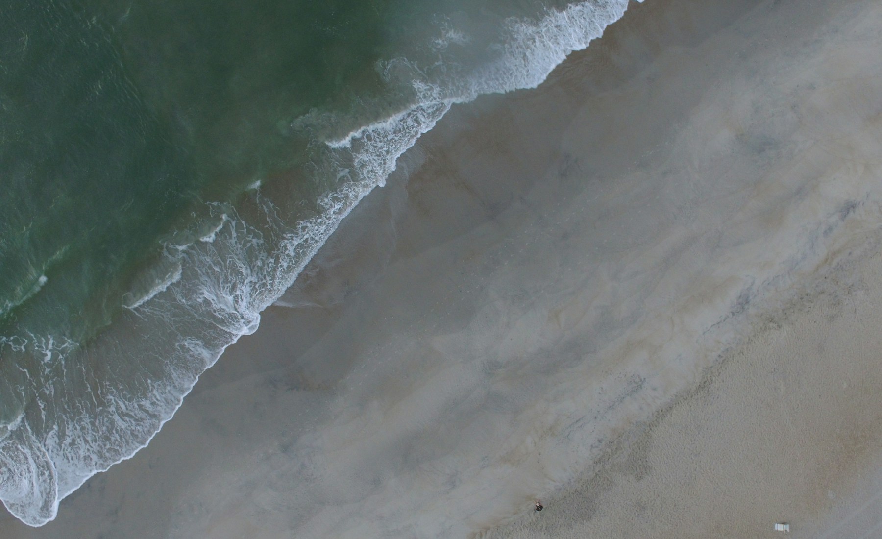 An aerial view of foamy waves reaching the sand at Wrightsville Beach